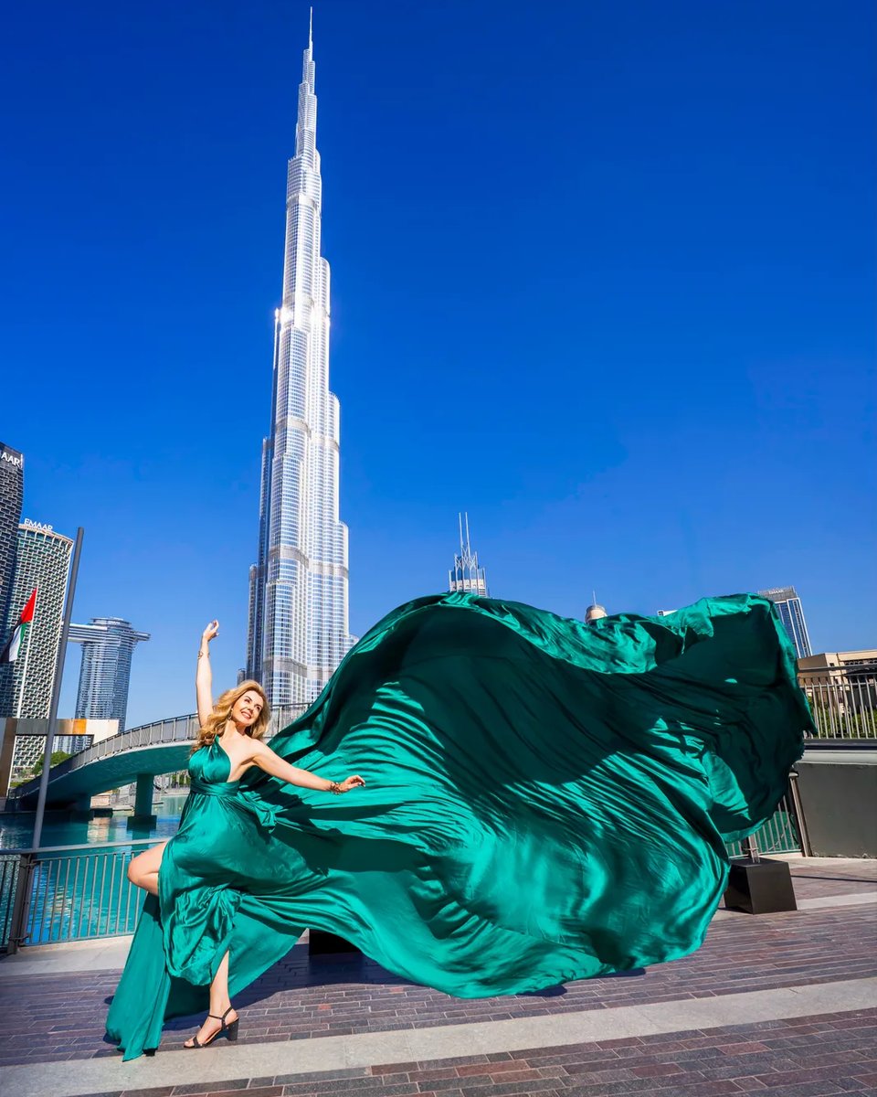 Emerald flying dress whipping sideways as a woman raises one arm and knee before Burj Khalifa