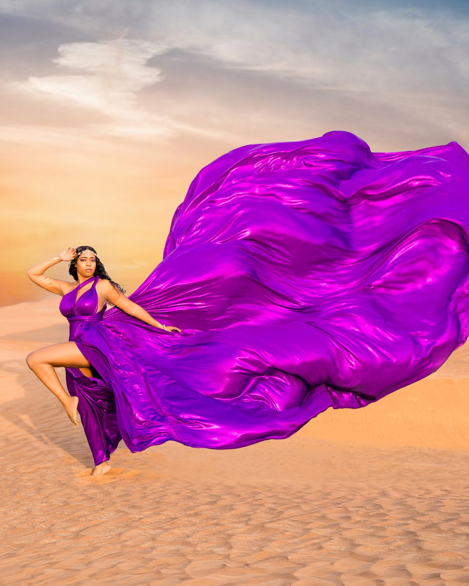 Purple flying dress billowing behind a woman posing on Dubai desert dunes at sunset