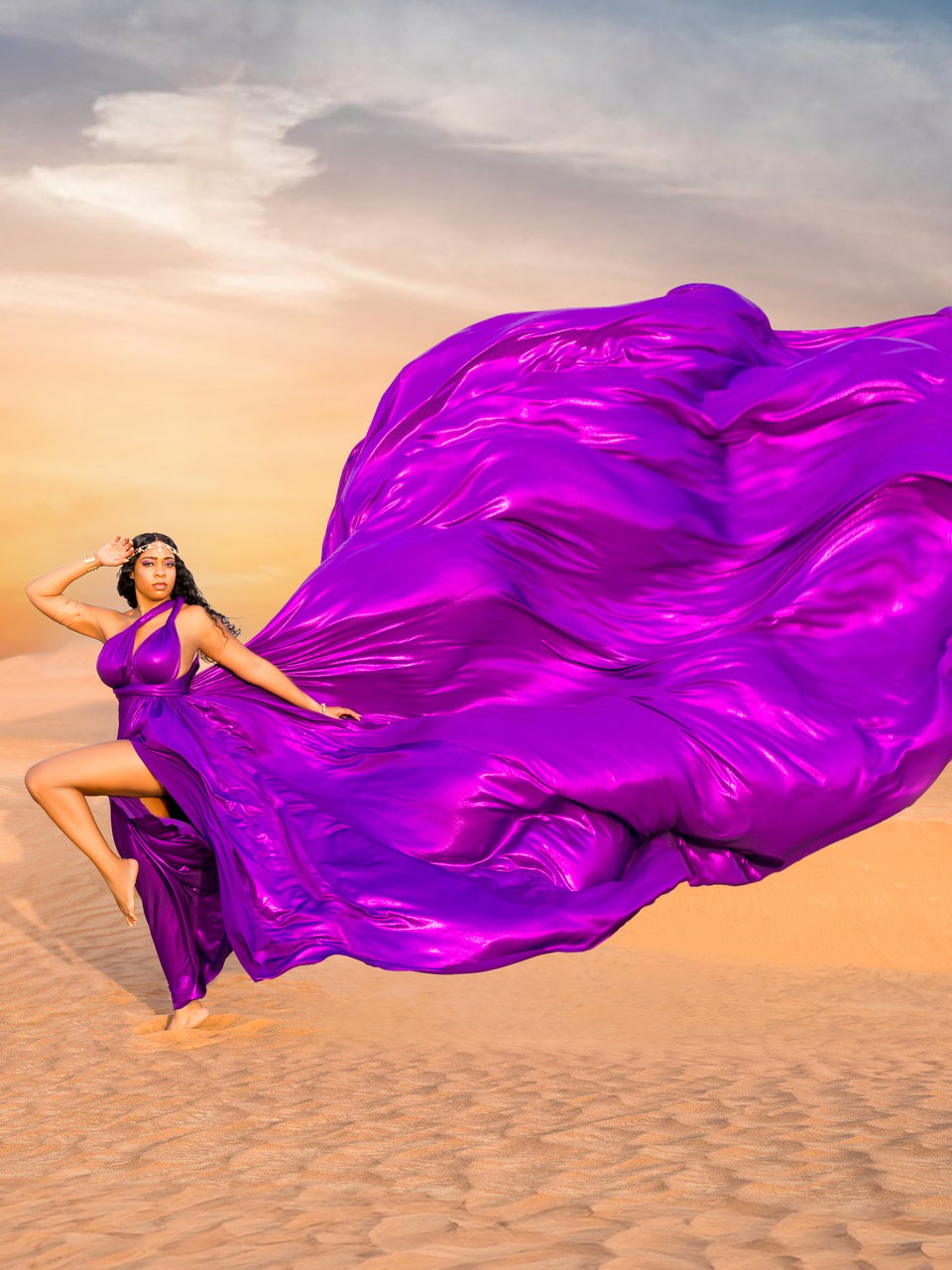 Purple flying dress billowing behind a woman posing on Dubai desert dunes at sunset