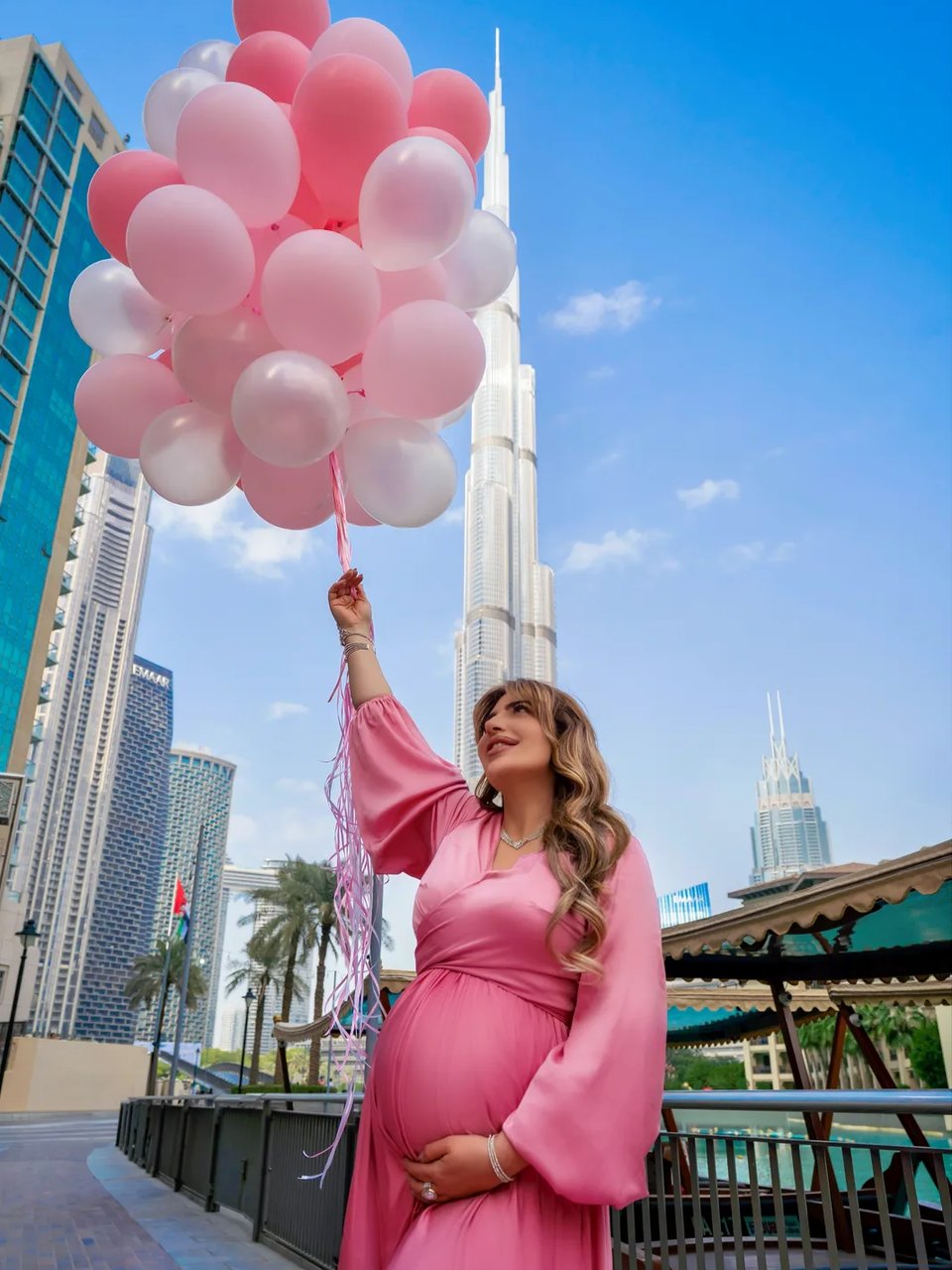 Pregnant woman in pink sleeved gown holding balloon cluster near the Burj Khalifa