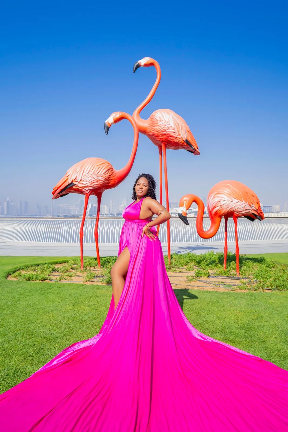 Fuchsia gown spread across green lawn among tall flamingo sculptures near the waterfront