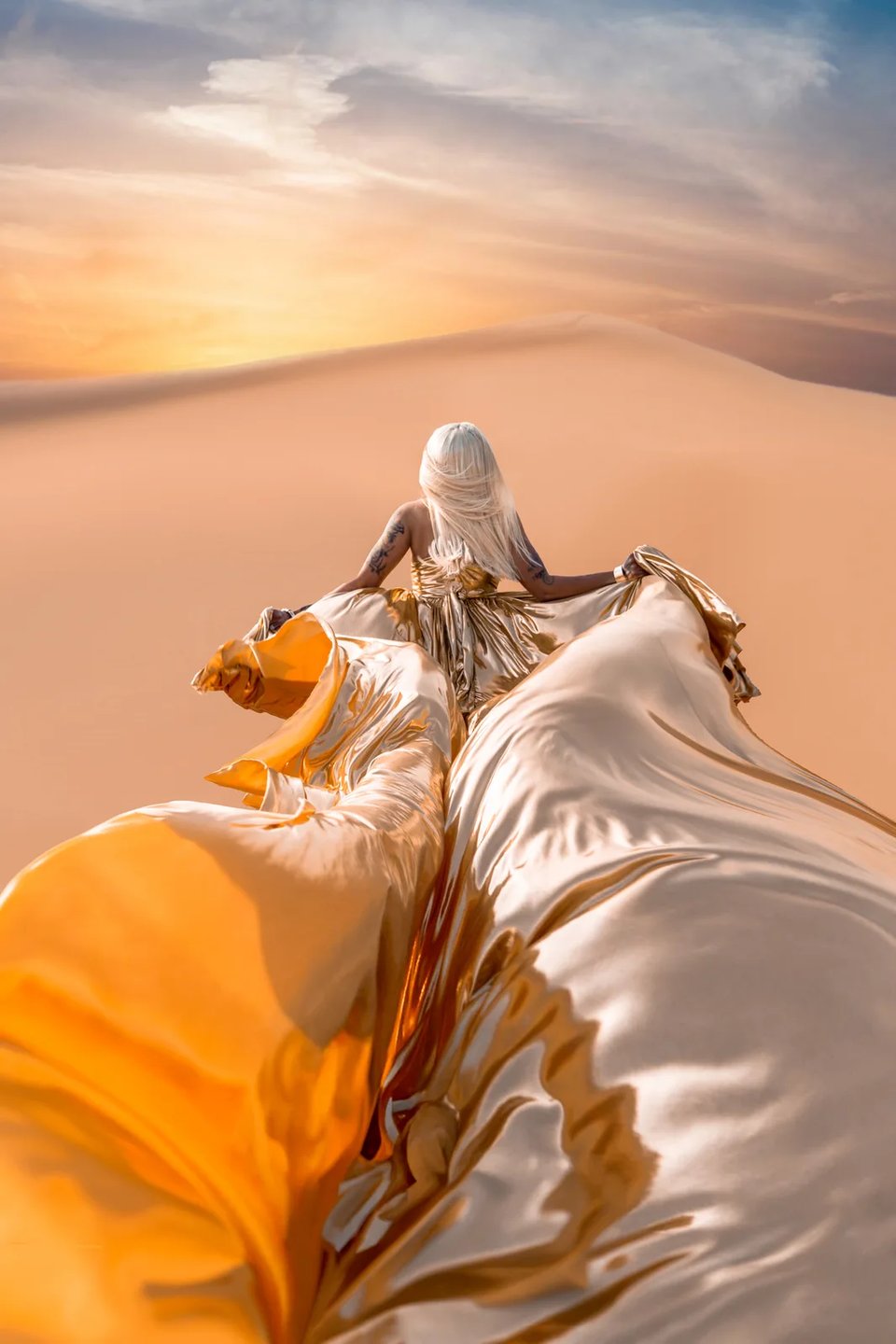 Champagne-gold flying gown with sweeping train trailing across golden desert dunes at sunset