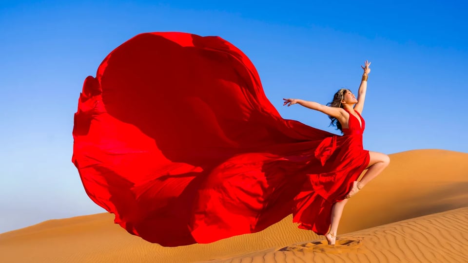 Red flying dress caught mid-air as she leaps barefoot across desert sand