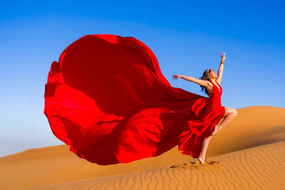 Red flying dress caught mid-air as she leaps barefoot across desert sand